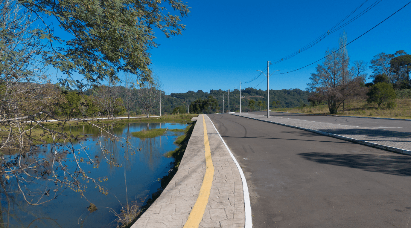 Life & Health — via de acesso ao empreendimento com lagoa ao fundo, infraestrutura viária e paisagem natural de Gramado, RS